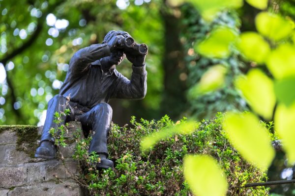 Sculpture of a man peering through binoculars set in a wooded space