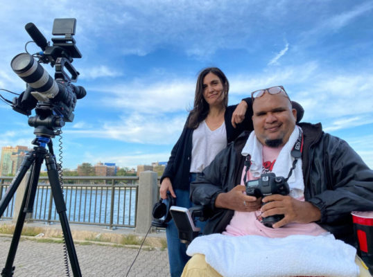 Two people holding film equipment are looking at the camera.