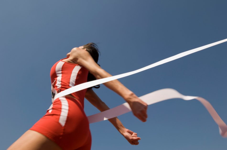 Low angle view of young female athlete crossing finish line against clear blue sky