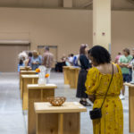 Visitors to North Charleston Arts Fest browse entries displayed on tables at Palmetto Hands in an indoor exhibition hall