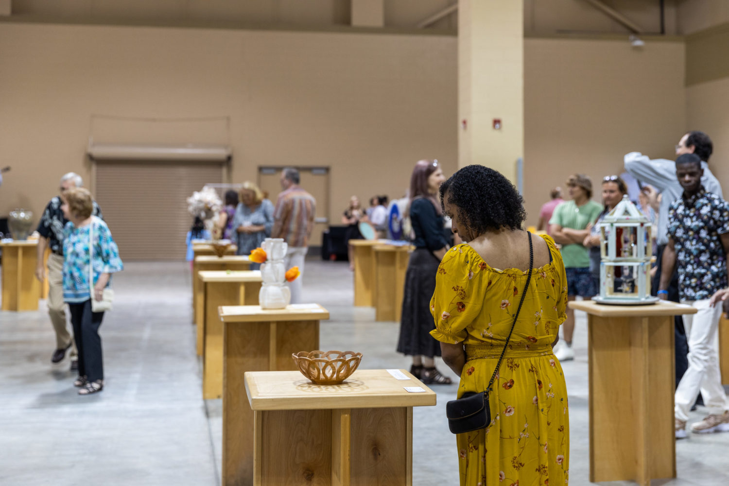 Visitors to North Charleston Arts Fest browse entries displayed on tables at Palmetto Hands in an indoor exhibition hall