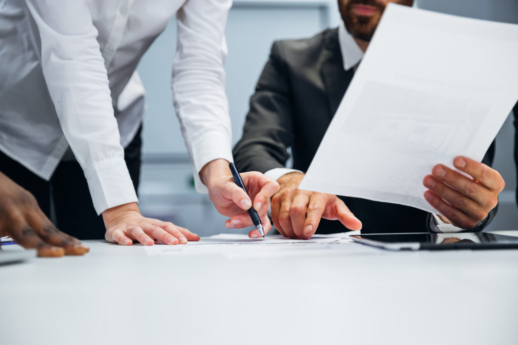 Arms and hands of three business people meeting at a table. One is holding a paper up to show the others.