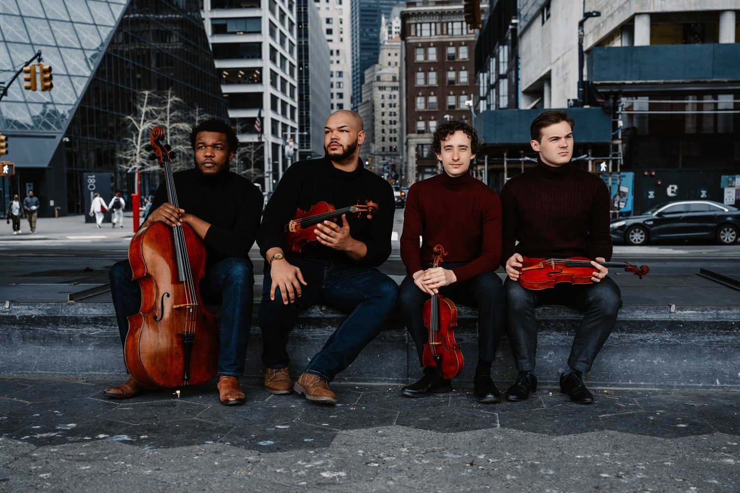 members of the Isidore String Quartet pose with their instruments on a city street