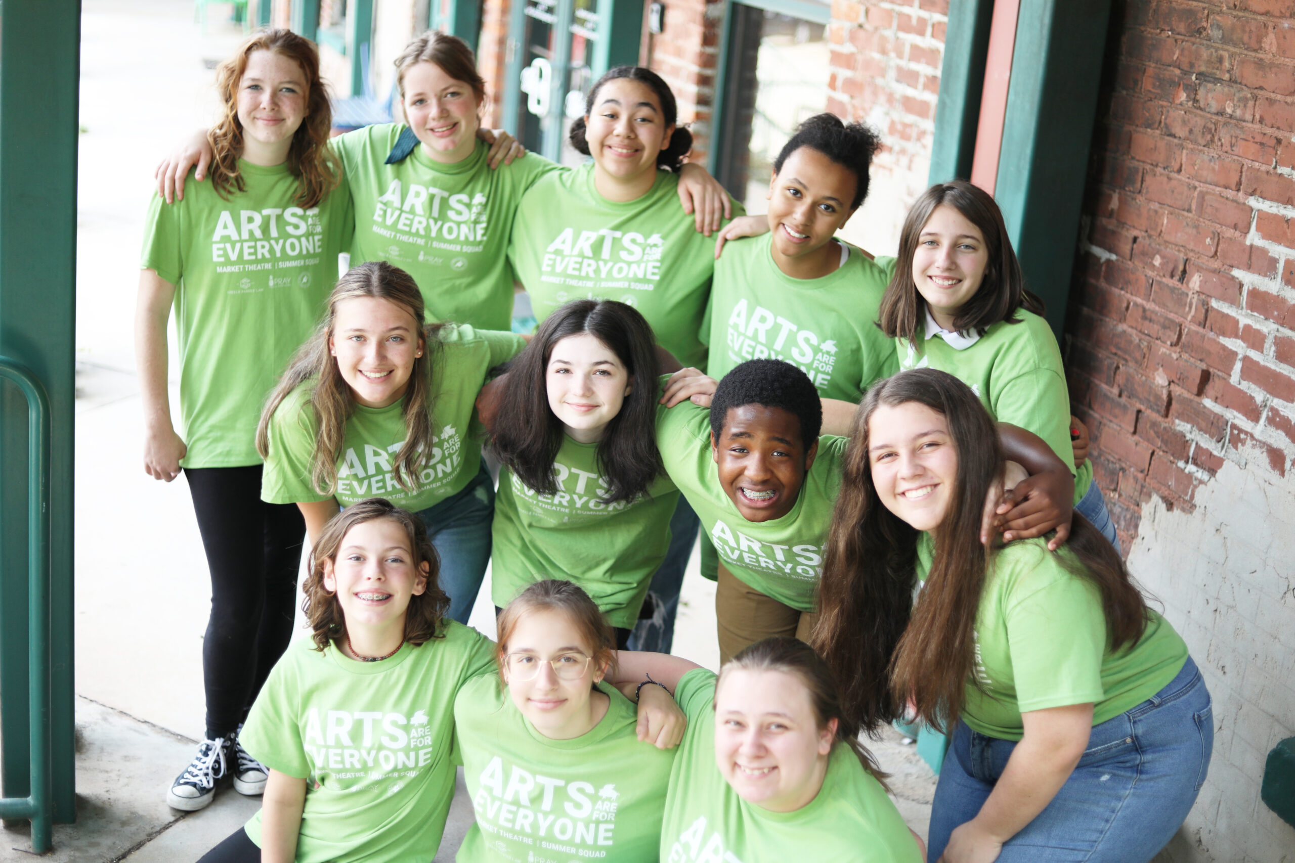 a group of smiling teens pose during a theatre camp, wearing shirts that read Arts Are for Everyone