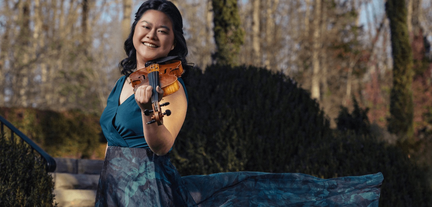 a smiling Asian-presenting woman holds her violin in playing position