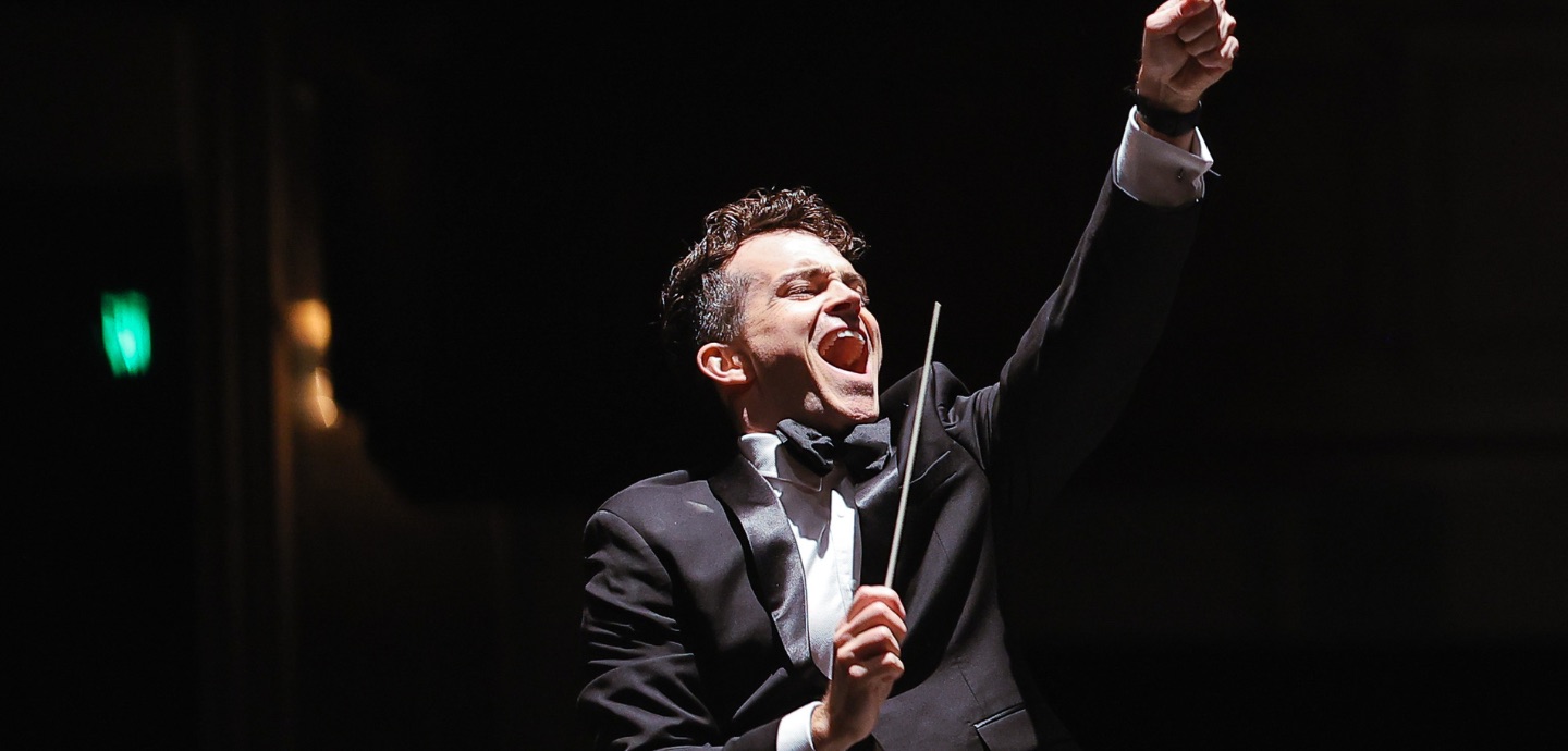 An excited man in formal dress conducts an orchestra.