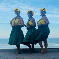 3 hula dancers in traditional garb on an ocean balcony