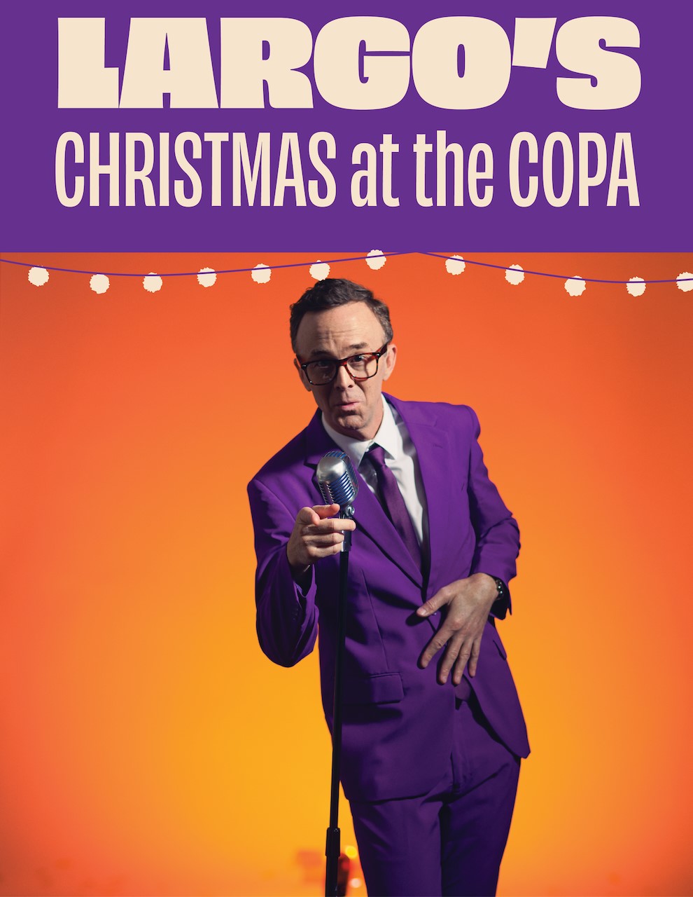 A man wearing glasses and a purple suit performs at an old-fashioned stand microphone.