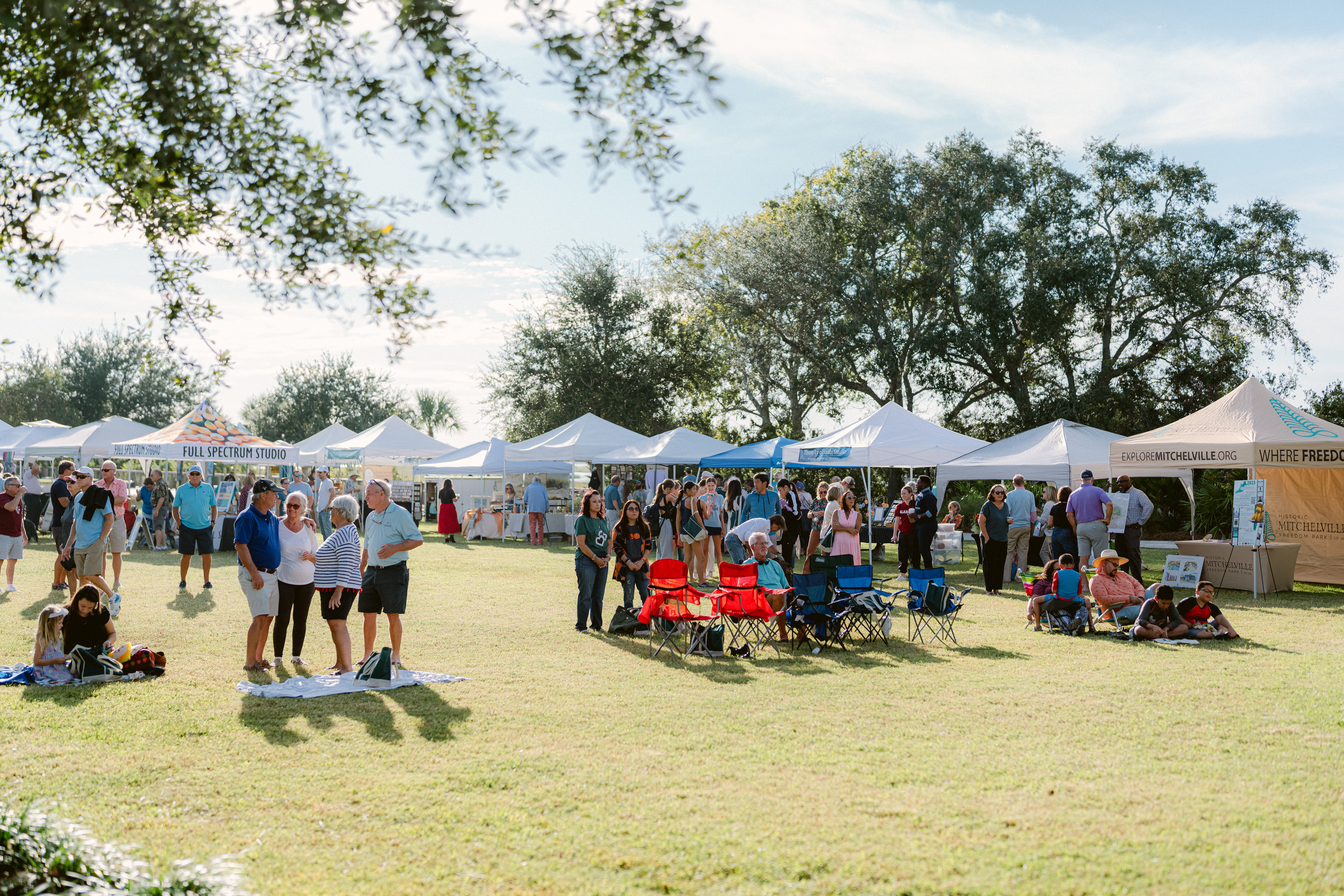 wide lawn with vendor tents and a small crowd of people setting up chairs and blankets for an event