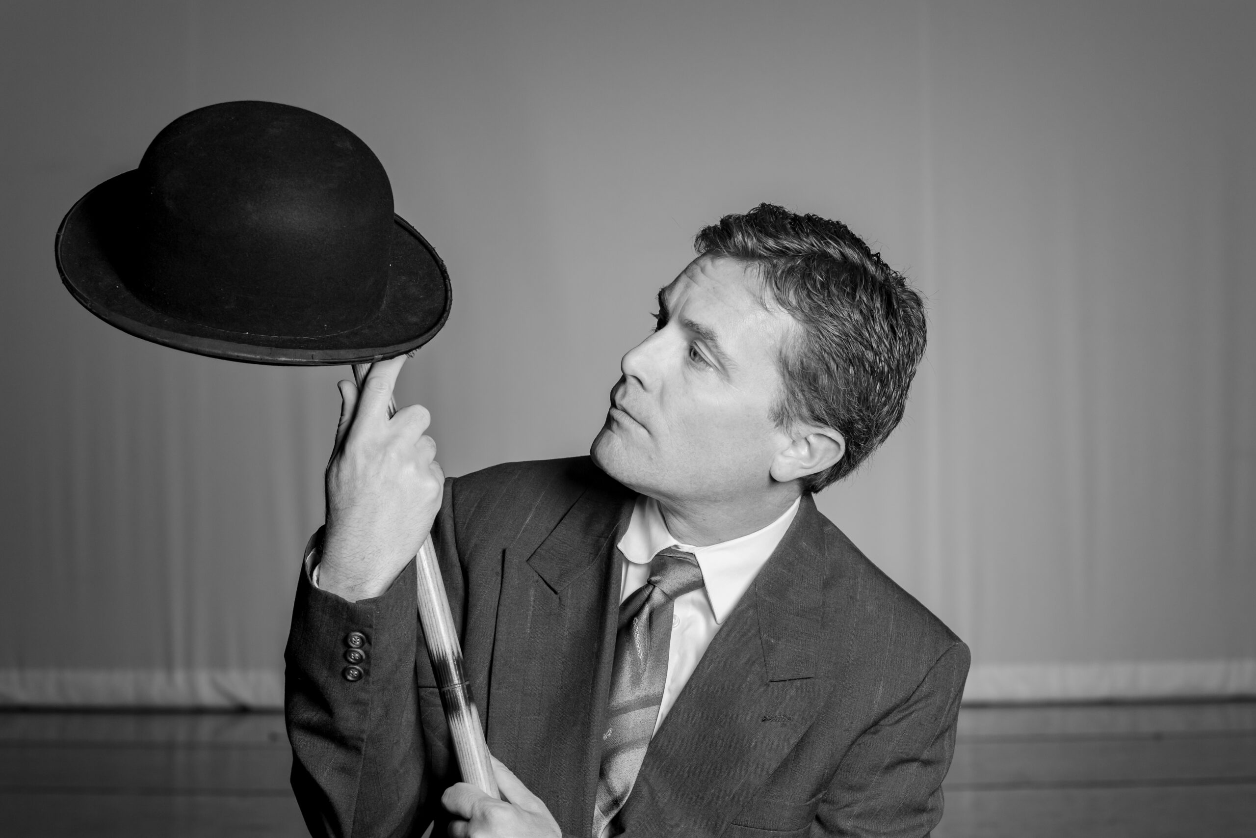 Performer Jeremy Meier studies a black bowler hat atop a cane.
