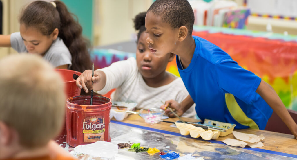 Children around a table in a school work with acrylic paints on a visual art project.