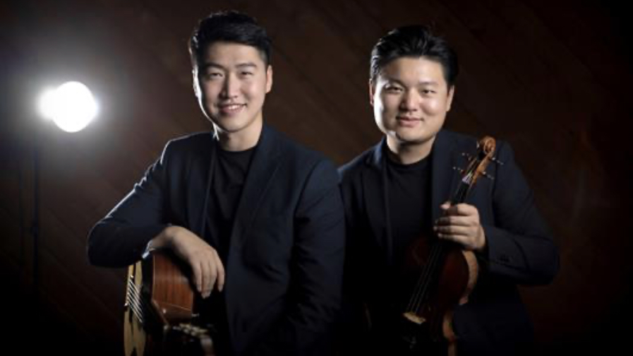 two smiling Asian people dressed in black, holding an acoustic guitar and a violin