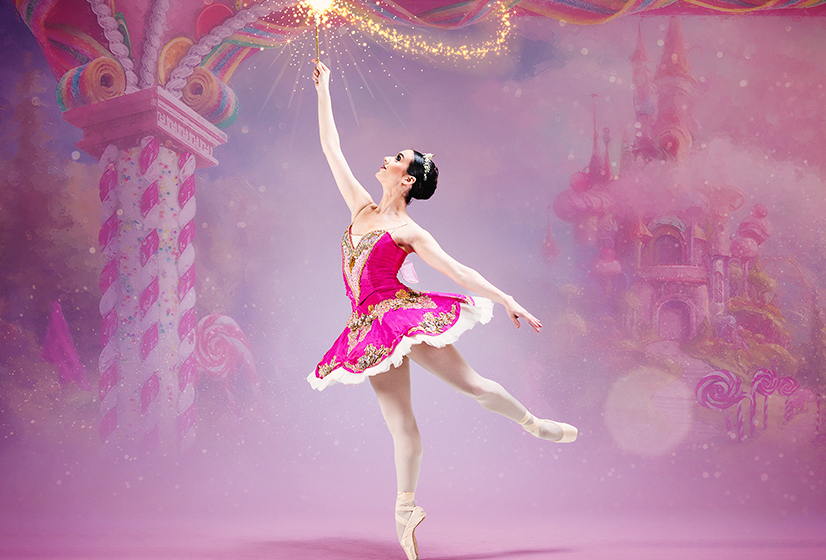 A ballet dancer en pointe in a pink tutu costume lifts a sparkling wand in a candy world