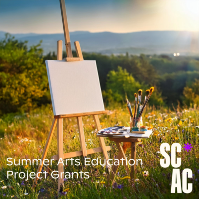 A painter's easel, paints and brushes are set up outdoors in a mountain meadow on a sunny summer day.