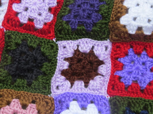 Crocheted granny squares in various colors including red, purple, black, green, white, and brown