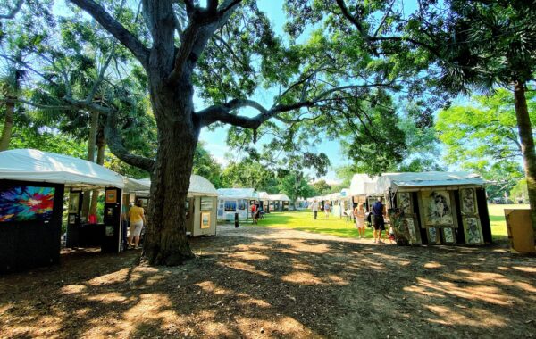 Rows of vendor tents set up on a grassy area under trees, with attendees browsing the artwork.