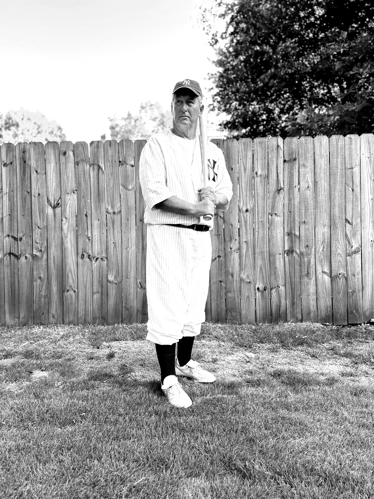 An actor as Babe Ruth, wearing a vintage New York Yankees uniform and holding a baseball bat.