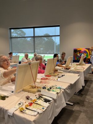 A group of older adults working on acrylic paintings in a classroom.