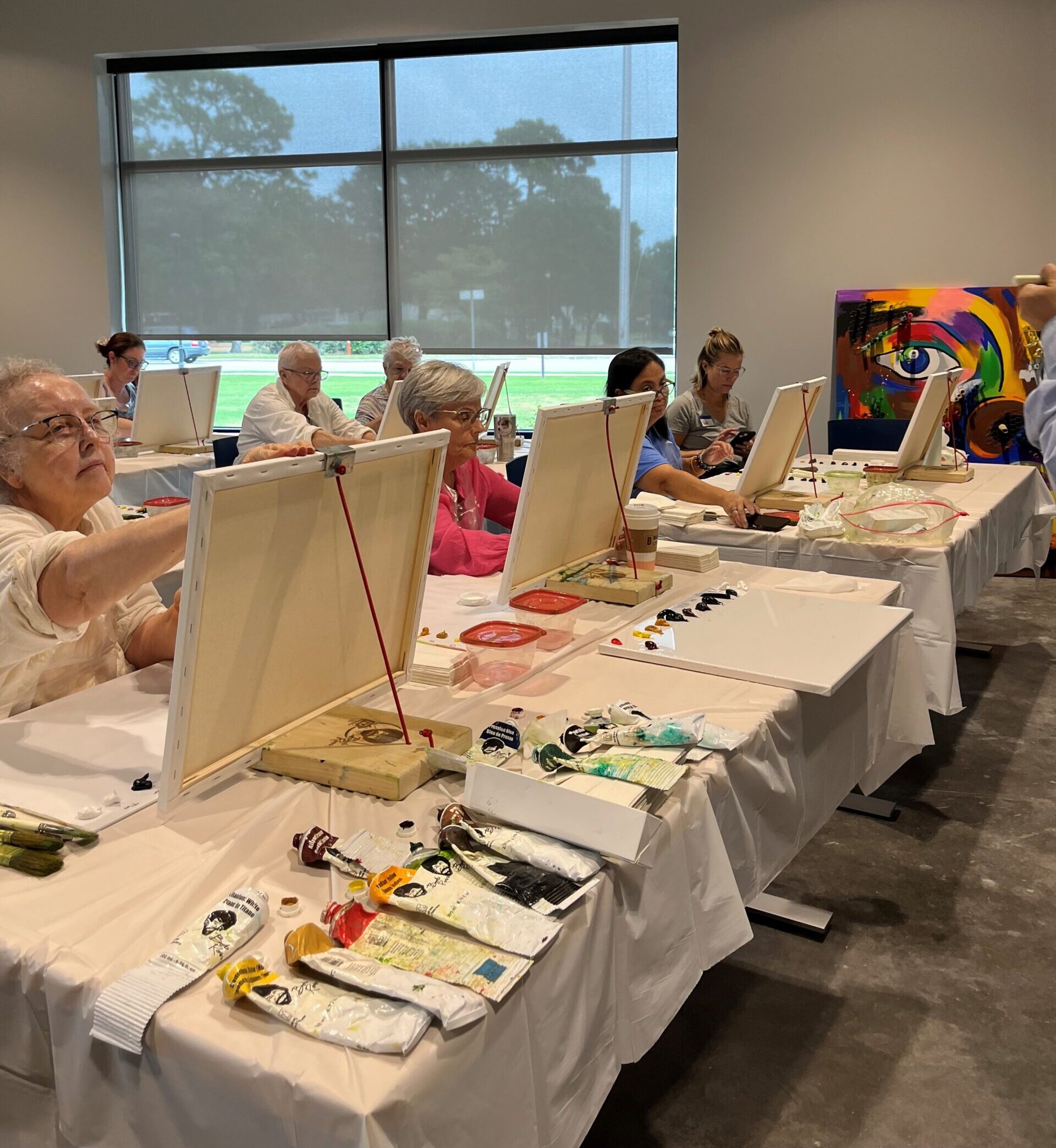 A group of older adults working on acrylic paintings in a classroom.