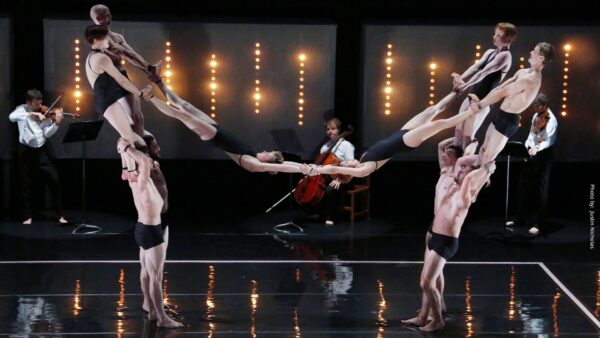 Onstage acrobats build a multi-level counter-balanced shape with a string quartet in the background.