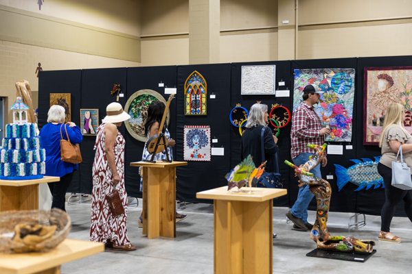Attendees at an art show view works on pedestals and on black fabric standing panels.