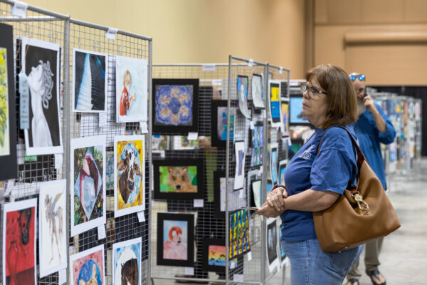 A person looks at youth artwork on paper, displayed on metal grids in an exhibit hall.