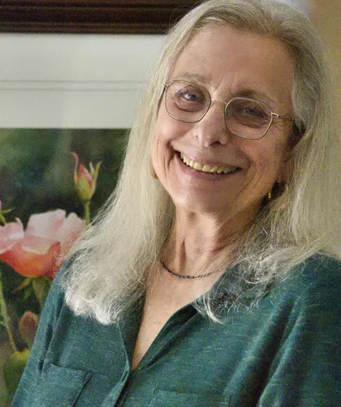 A woman with shoulder-length gray hair and glasses smiles at the viewer.