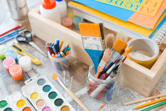 Art supplies, including paint, brushes, scissors, colored pencils, markers, and colored paper.