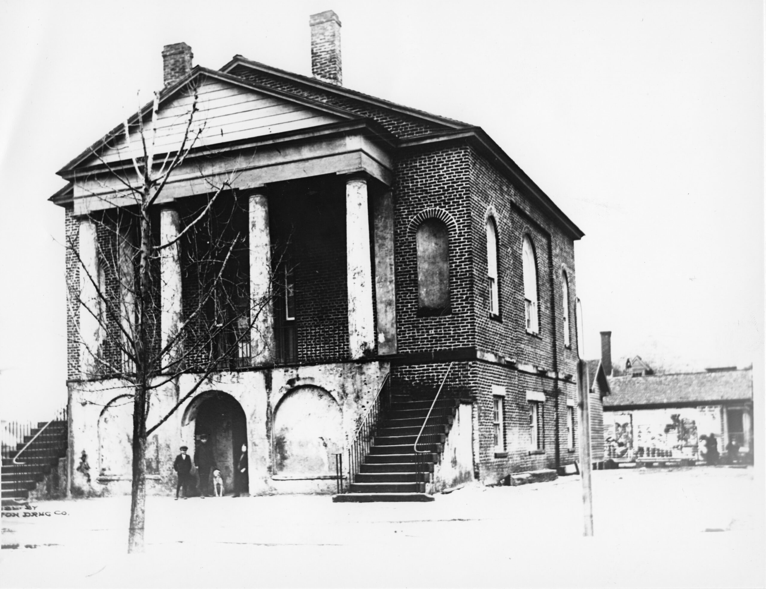 Two-story brick building with stairs leading to a portico with large columns.