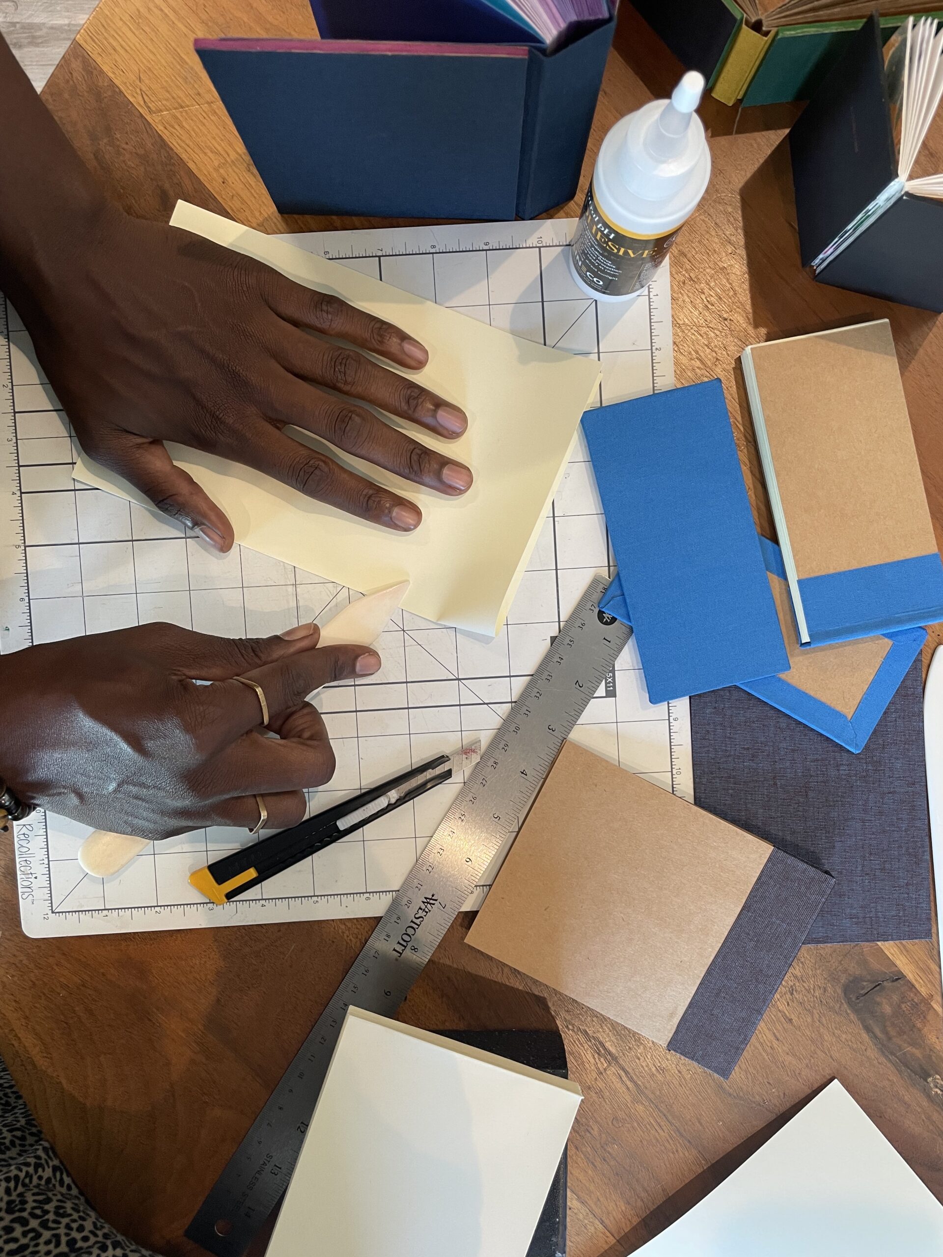 A Black person&#039;s hands work with paper and tools on a gridded cutting mat.