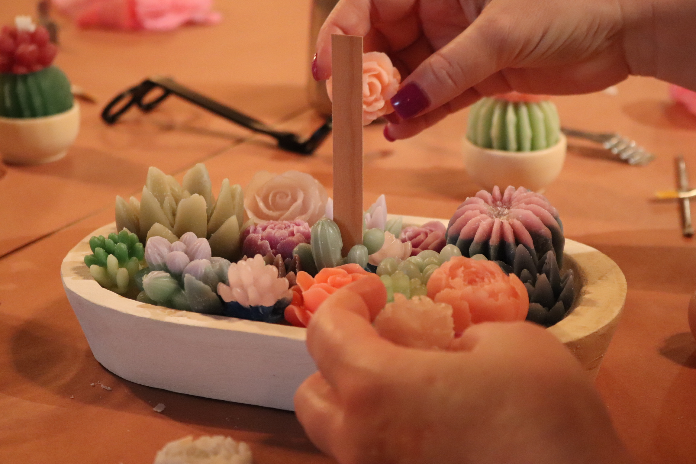 A woman's hands assemble a shallow dish of miniature succulents made of wax.