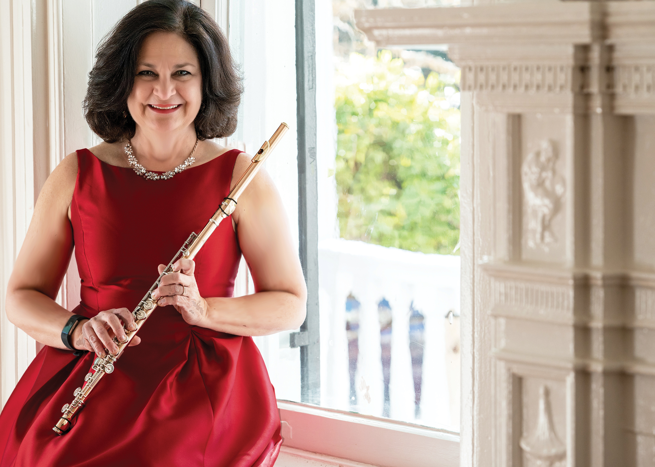 A woman with dark hair in formal dress sits on a windowsill holding her flute.