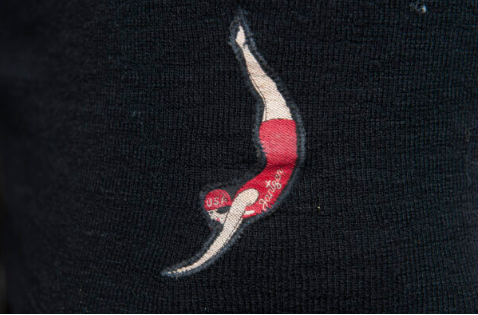 Fabric appliqué of a woman diving. She wears a red swim cap and an old-fashioned red swimsuit.
