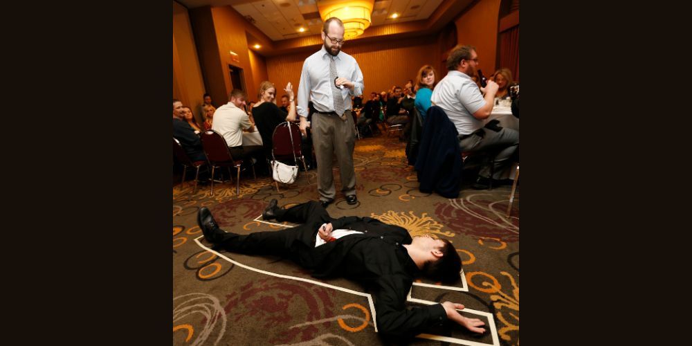 A murder mystery actor lies on the floor surrounded by a masking tape outline.