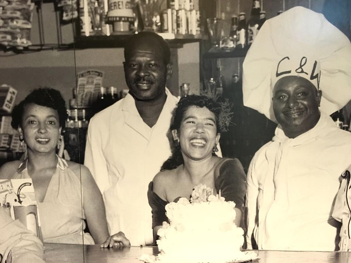 Four Black individuals smiling at a counter. One man wears a chef's hat with "C & W" written on it.