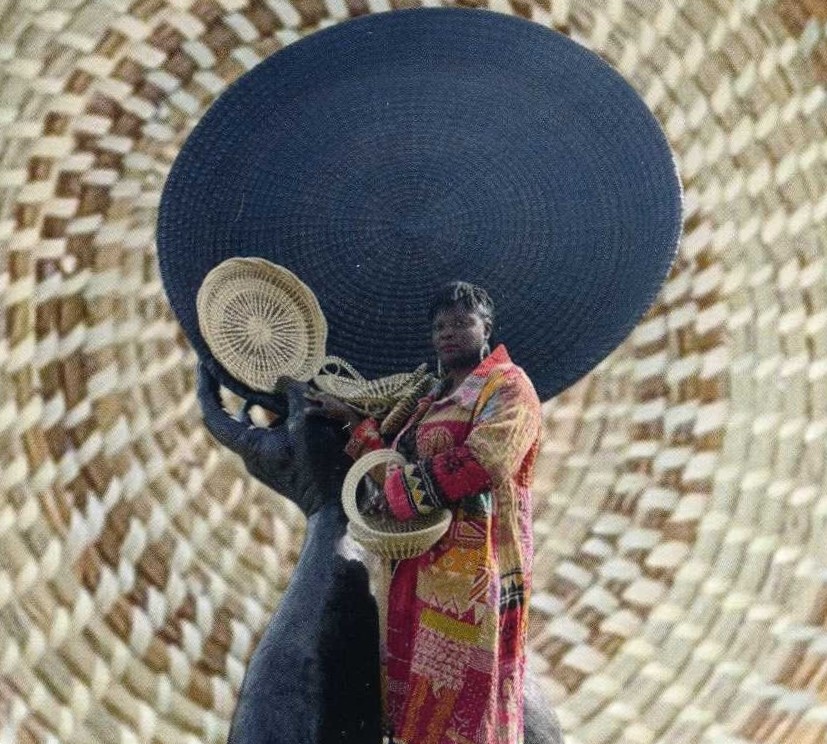 A Black woman in a colorful coat displays sweetgrass baskets.