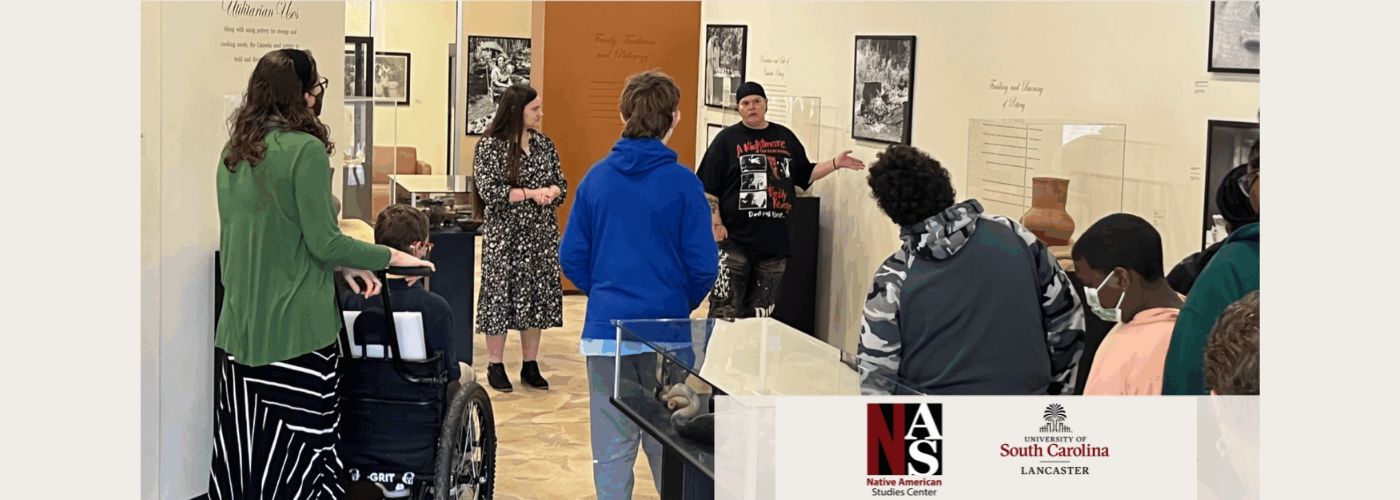 People on a guided museum tour. They vary in age, gender, and race. One sits in a wheelchair.