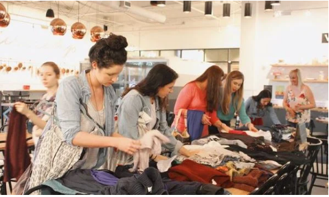 A group of women looking through piles of clothes on tables.