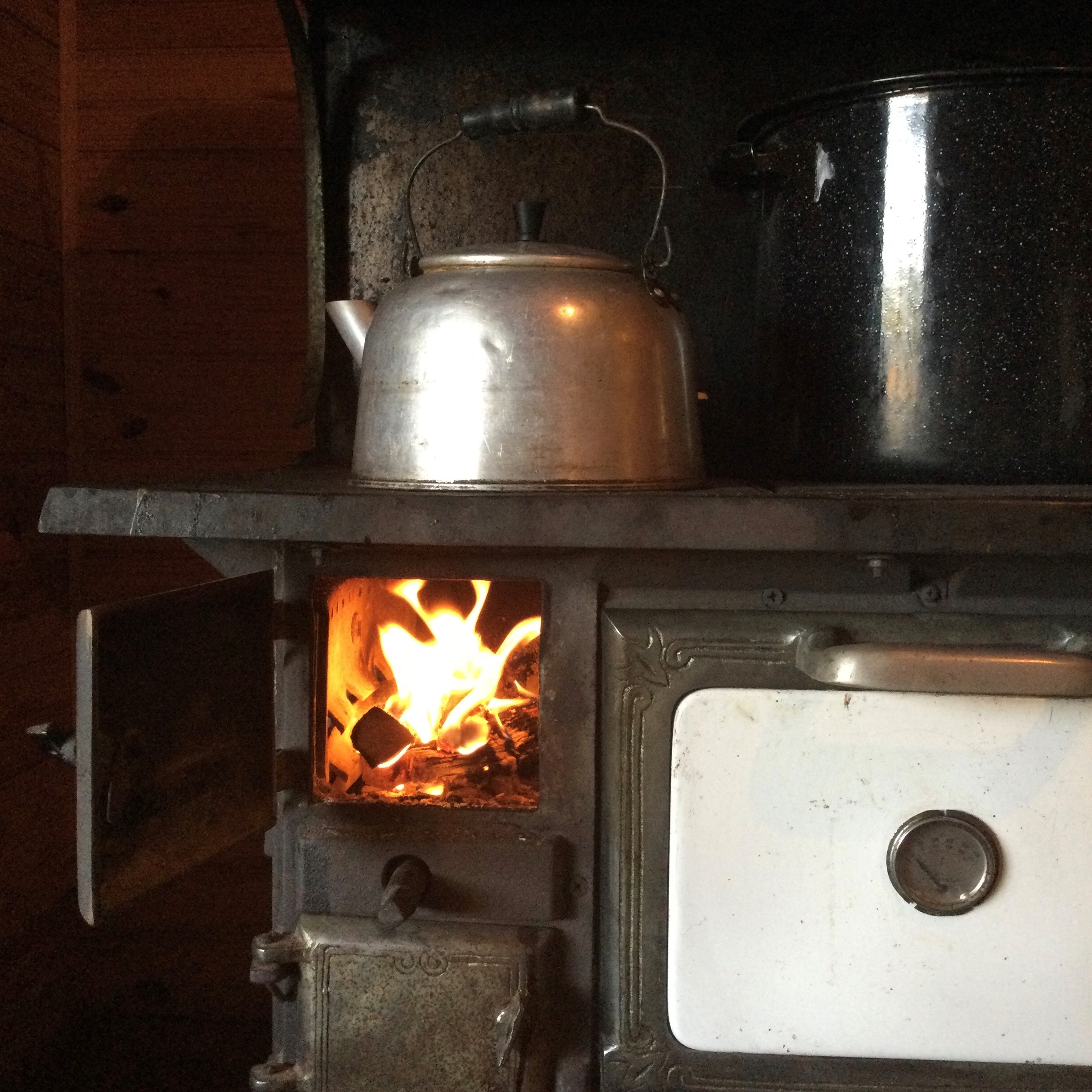 A kettle sits atop a lit wood-burning stove.