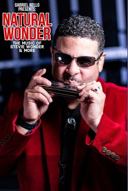 An artist presenting as BIPOC male wears sunglasses and plays a harmonica.