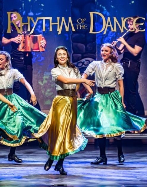 Three women in traditional Irish dance attire perform on a stage.