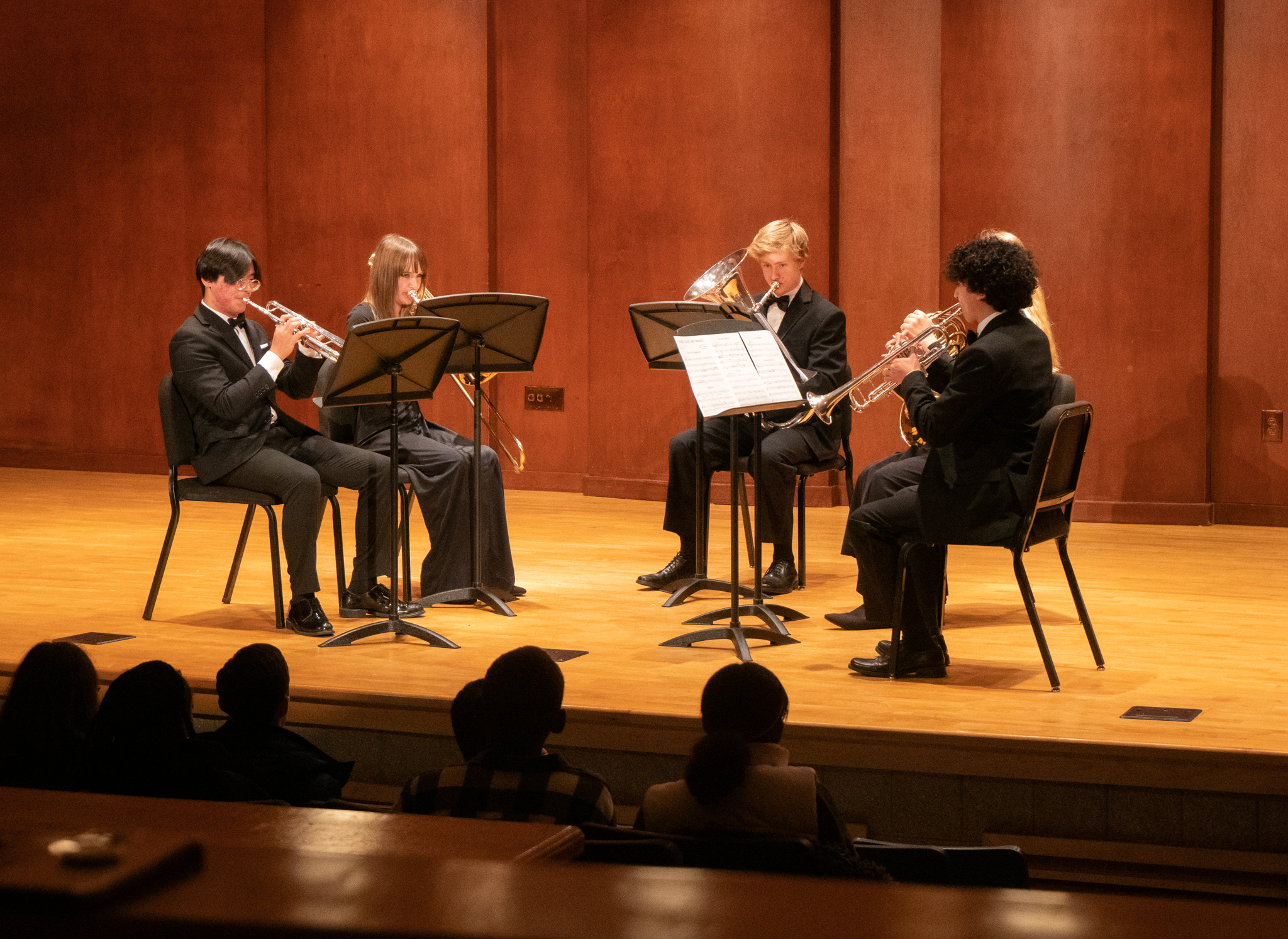 A student brass quintet performs on a formal wooden stage.
