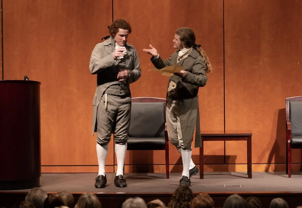 Historical interpreters dressed in clothing of the American Revolutionary War era, on stage.