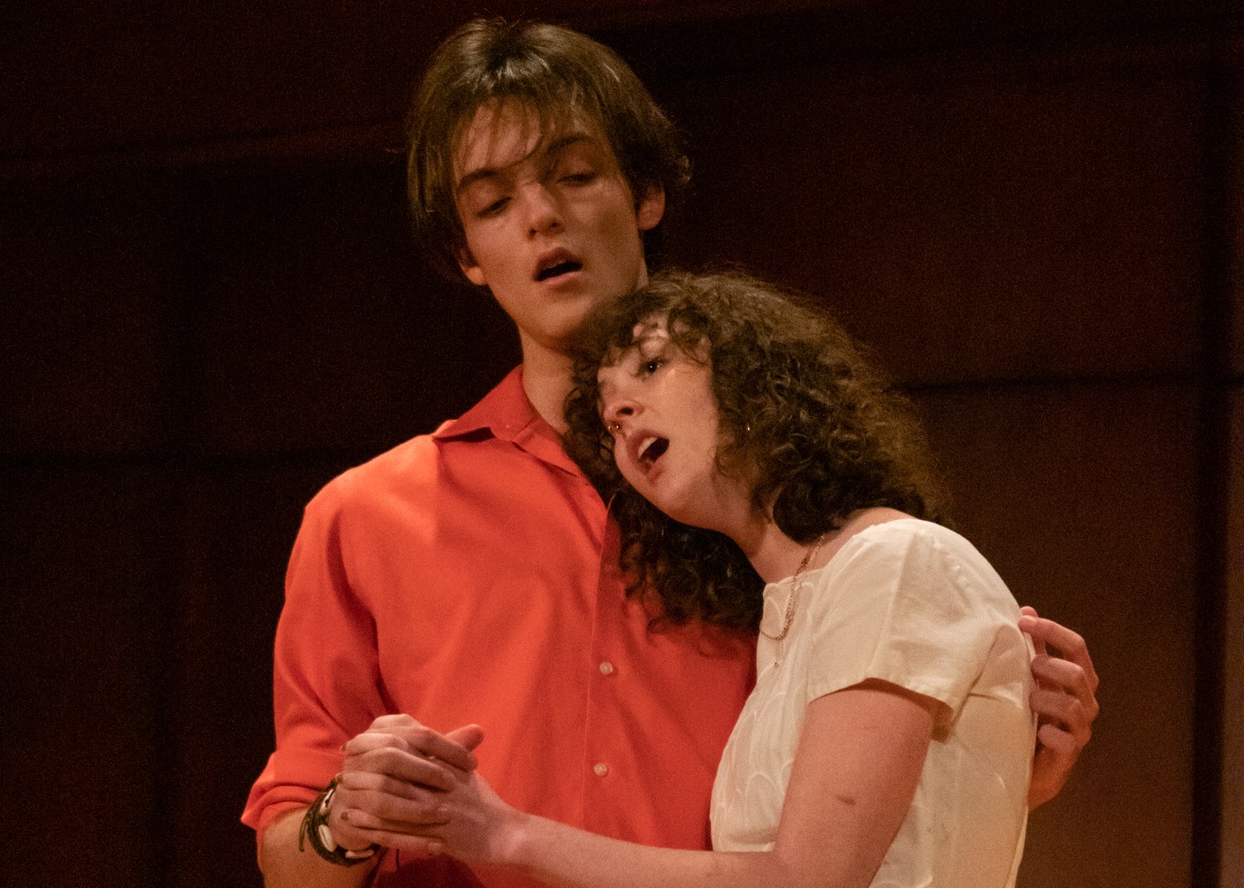 A male student and a female student embrace in a vocal performance.