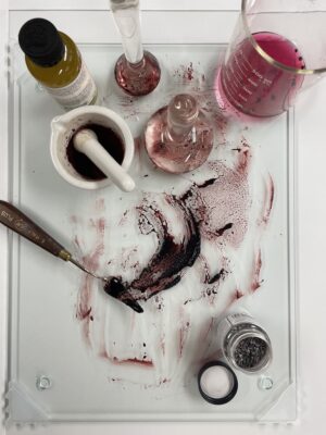 Tools for creating paint, including a mortar and pestle, beaker, water, pigments, and palette knife.