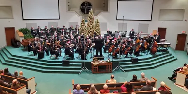 A seated orchestra performs on a large altar stage area at the front of a church.
