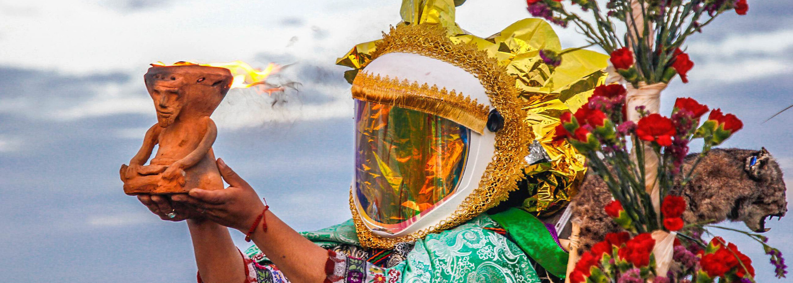 A person in a decorative helmet holds a small terra cotta figure with flame exiting the top.
