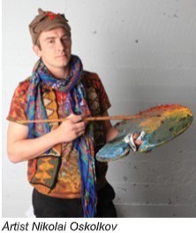 A young man in a multicolored shirt and scarf, holding a brush and palette loaded with paint.