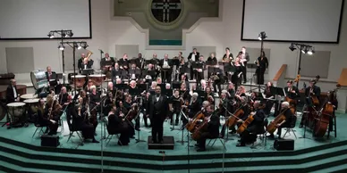 An orchestra is seated on large altar stage area at the front of a church.