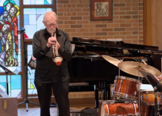 An older gentleman plays a muted trumpet in a church setting.